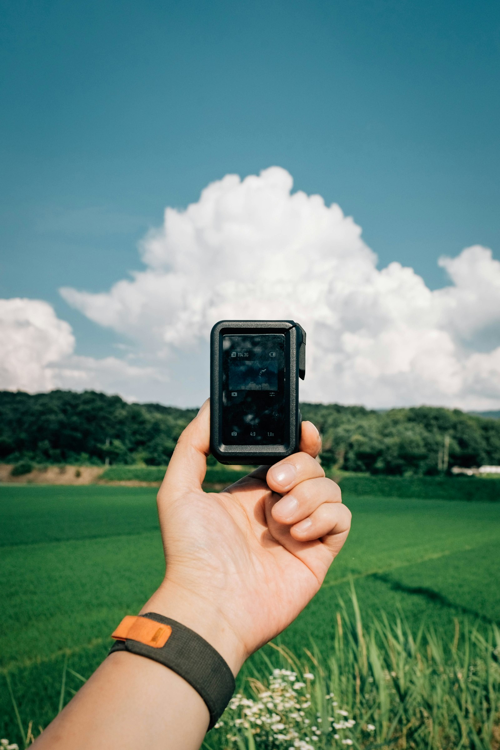 Hand holding a golf rangefinder on a golf course under a cloudy sky